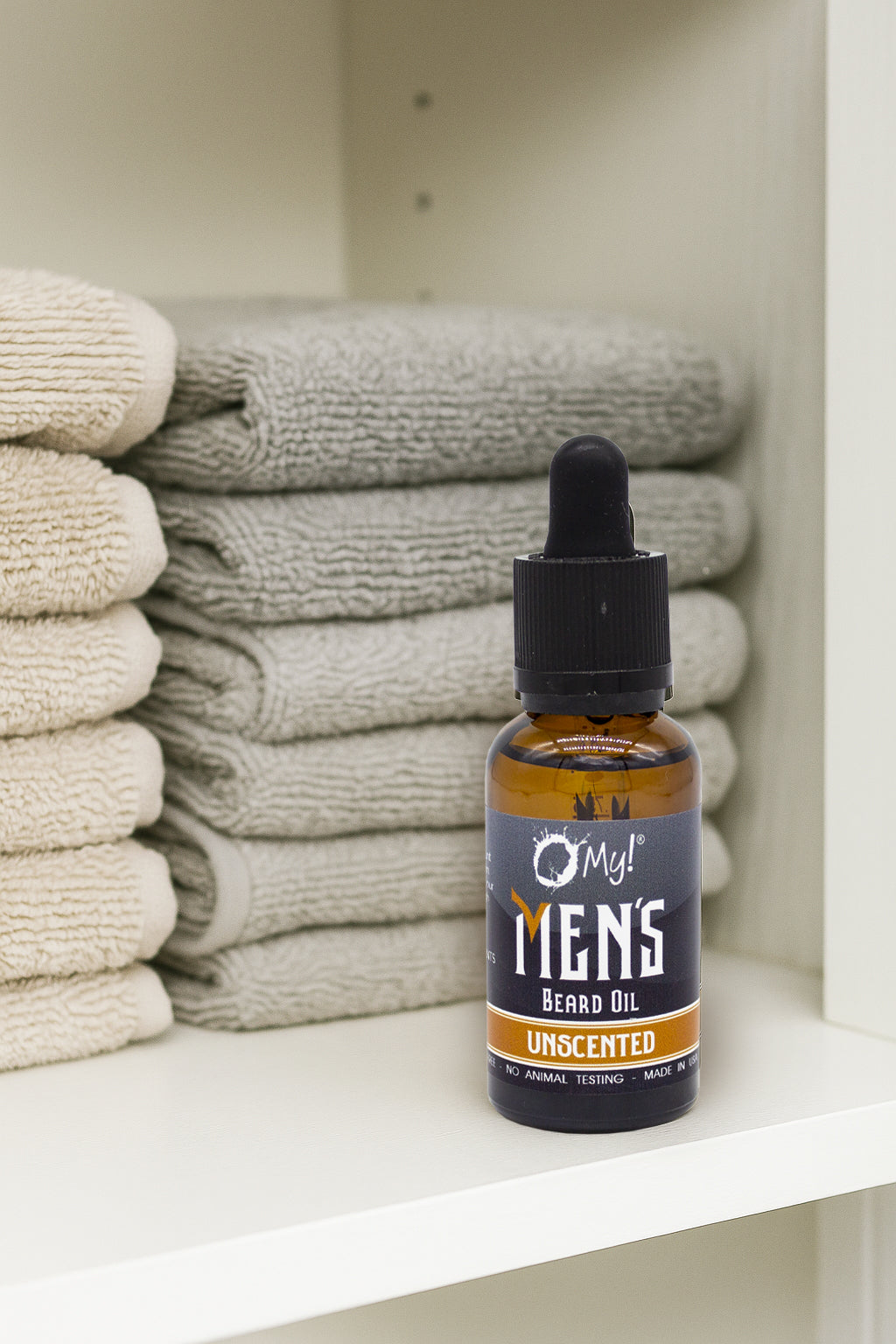 Bottle of O My! Men's Unscented Beard Oil on a shelf with folded towels