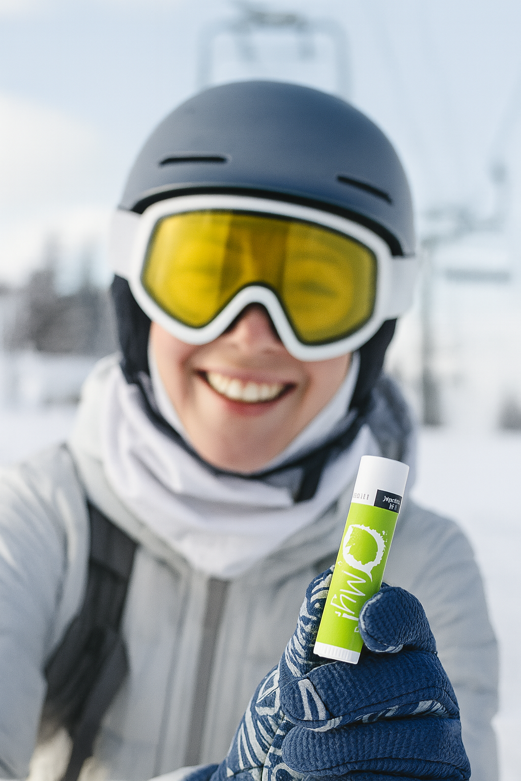 Person in winter gear holding an O My! Goat Milk Lip Balm with a snowy background