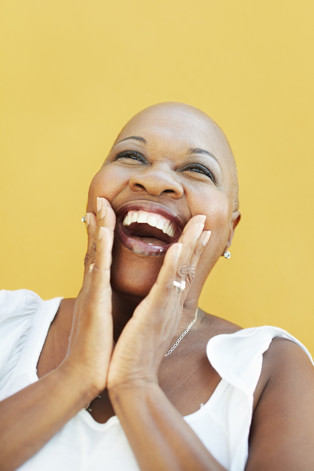 Bald woman laughing with hands on cheeks against a yellow background