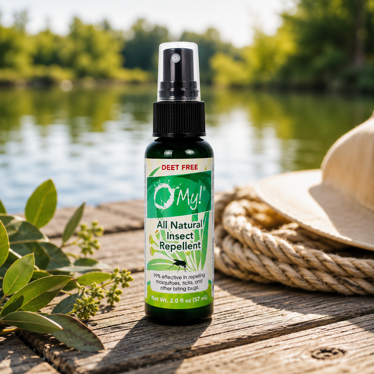 A bottle of O Myl All Natural Insect Repellent standing on a wooden deck outdoors with a lake and trees in the background, next to a straw hat and green leaves.