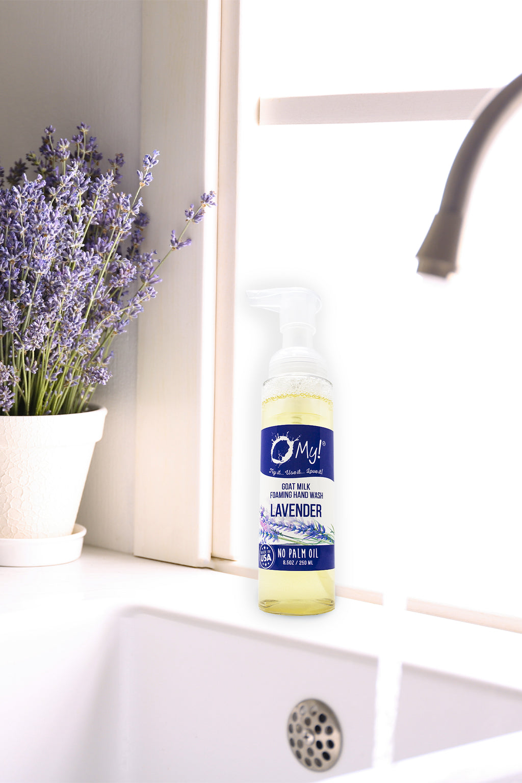 Bottle of OMy! Lavender body wash on a bathroom counter with lavender flowers in the background.