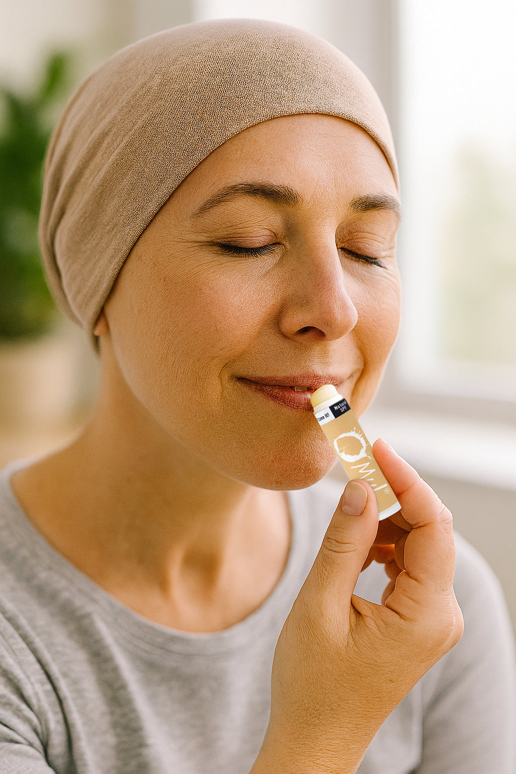 Woman going through chemo is applying lip balm with a neutral background