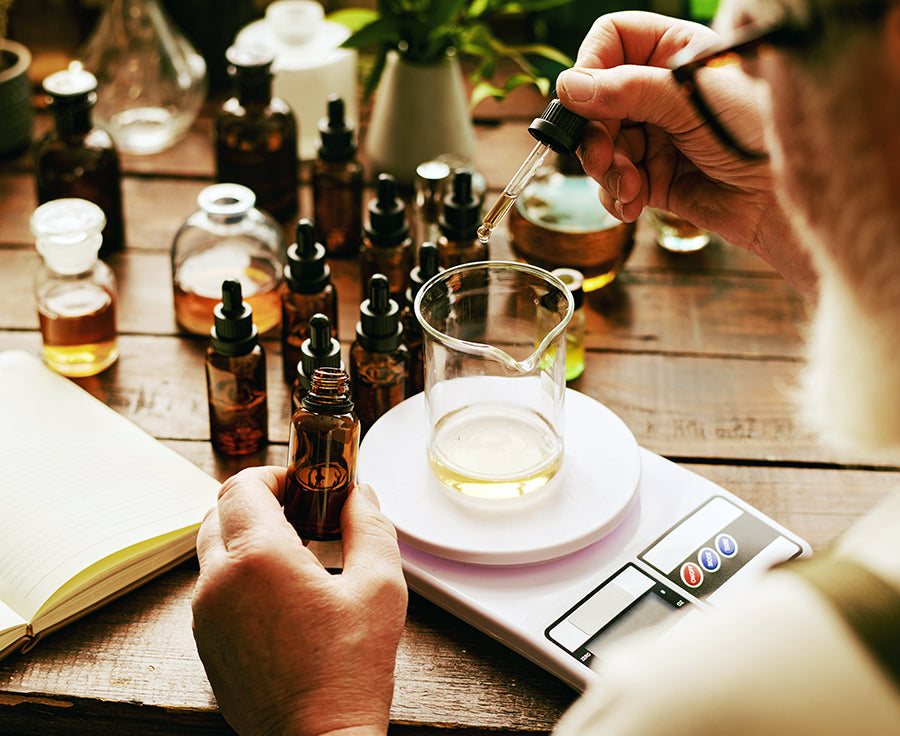 O My! Bath and Body Person combining essential oils with various bottles and a beaker on a wooden table.