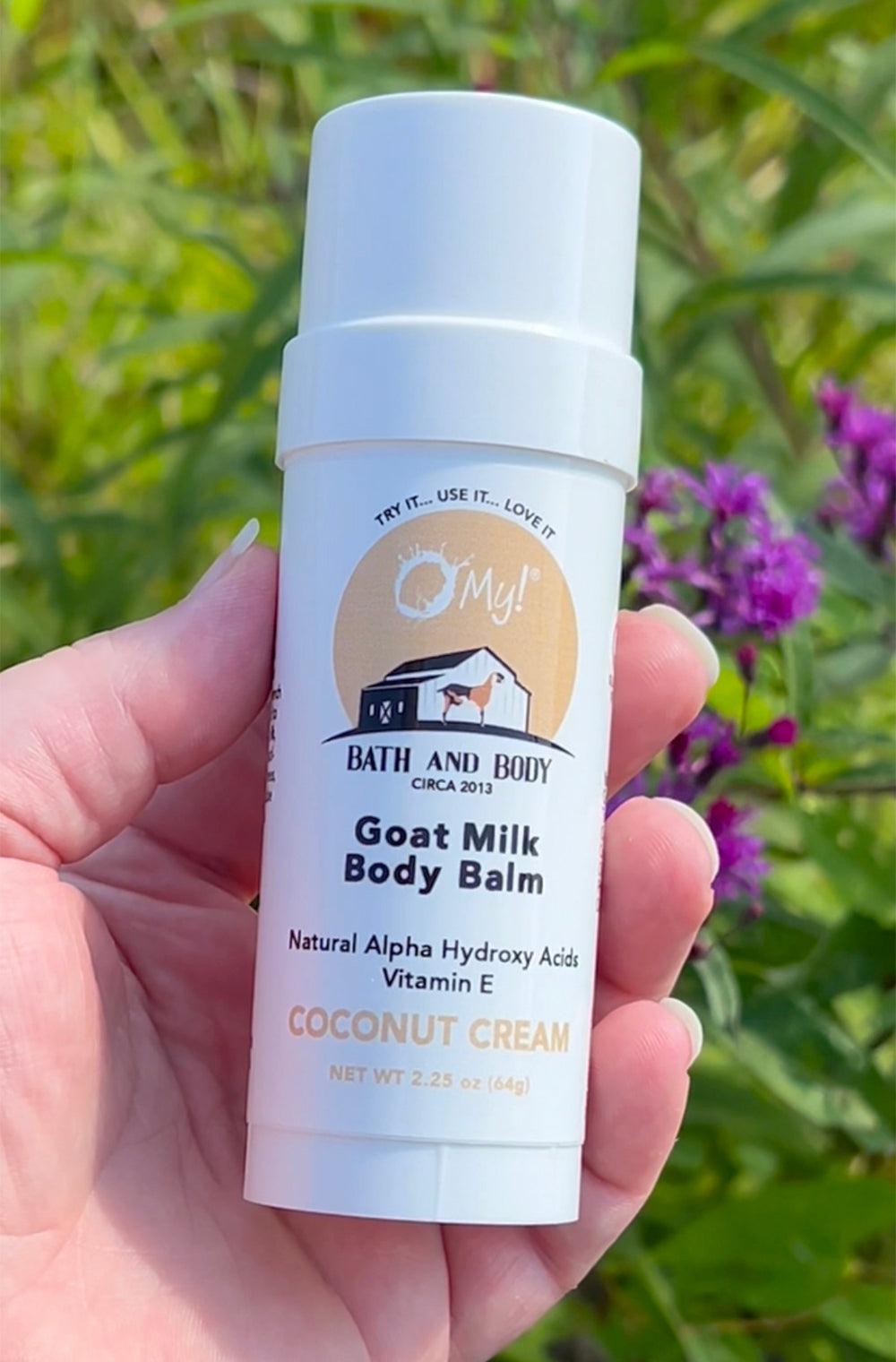O My! Goat Milk Body Balm Coconut Cream being held in front of a backdrop of lavender.