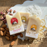 Three O my! goat milk traveler soap bars with visible branding on a wooden surface with almonds and oats.