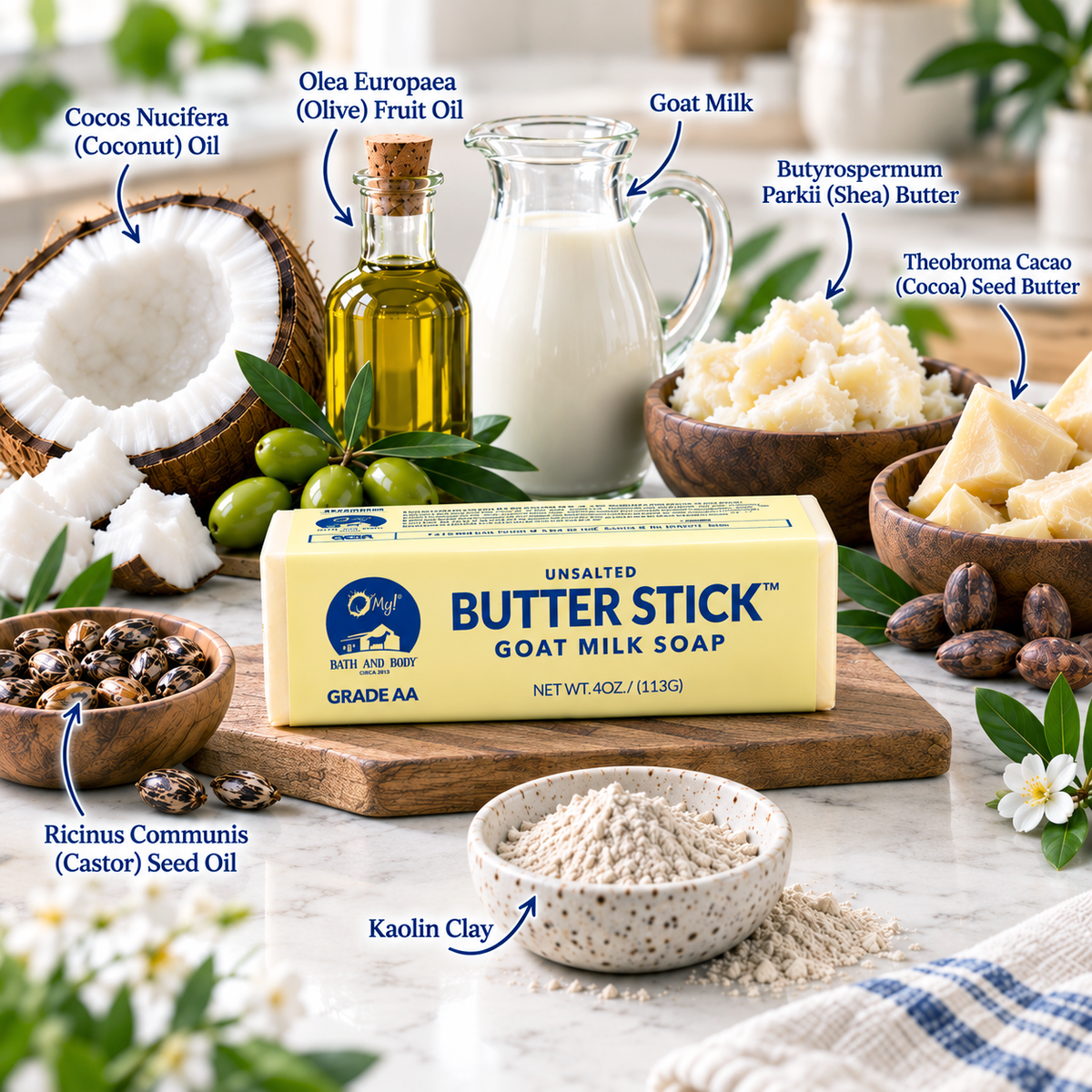 An O My! Butter Stick goat milk soap is centered on a wood surface, surrounded by labeled ingredients including coconut oil, olive fruit oil, goat milk, shea butter, cocoa seed butter, castor oil, kaolin clay, and cococ nucifera coconut. The butter stick  reads O My! Butter Stick Goat Milk Soap, Grade AA.