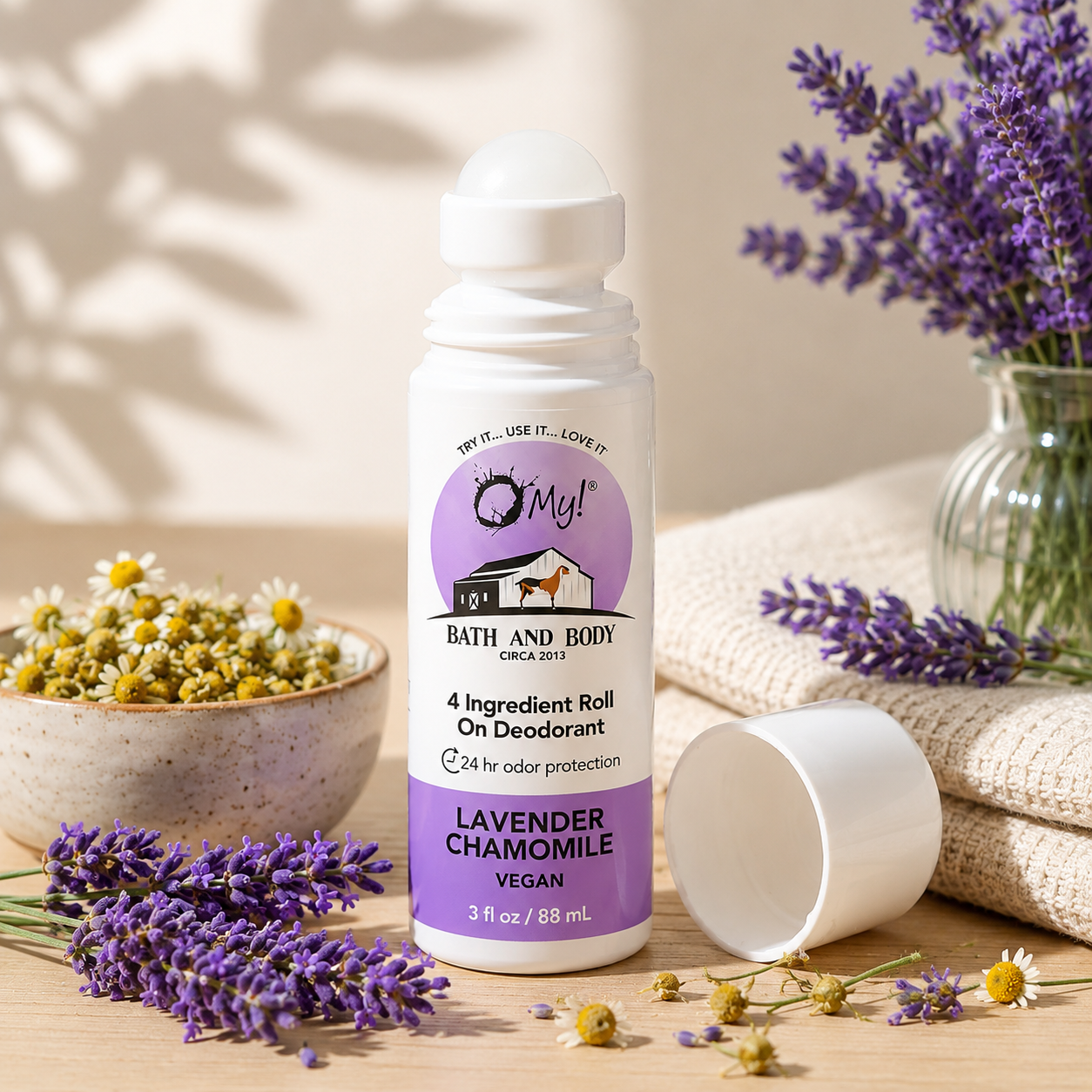 O My! 4 Ingredient Roll-on deodorant with lavender and chamomile on a wooden surface with flowers and towels.