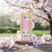O My Cherry Blossom goat milk soap bar with packaging on a wooden surface with cherry blossoms in the background