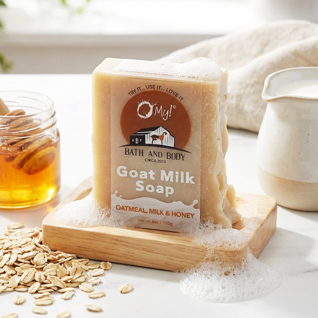 Bar of O My! goat milk soap with oatmeal, milk, and honey on a soap dish with bubbles, honey and milk around it.