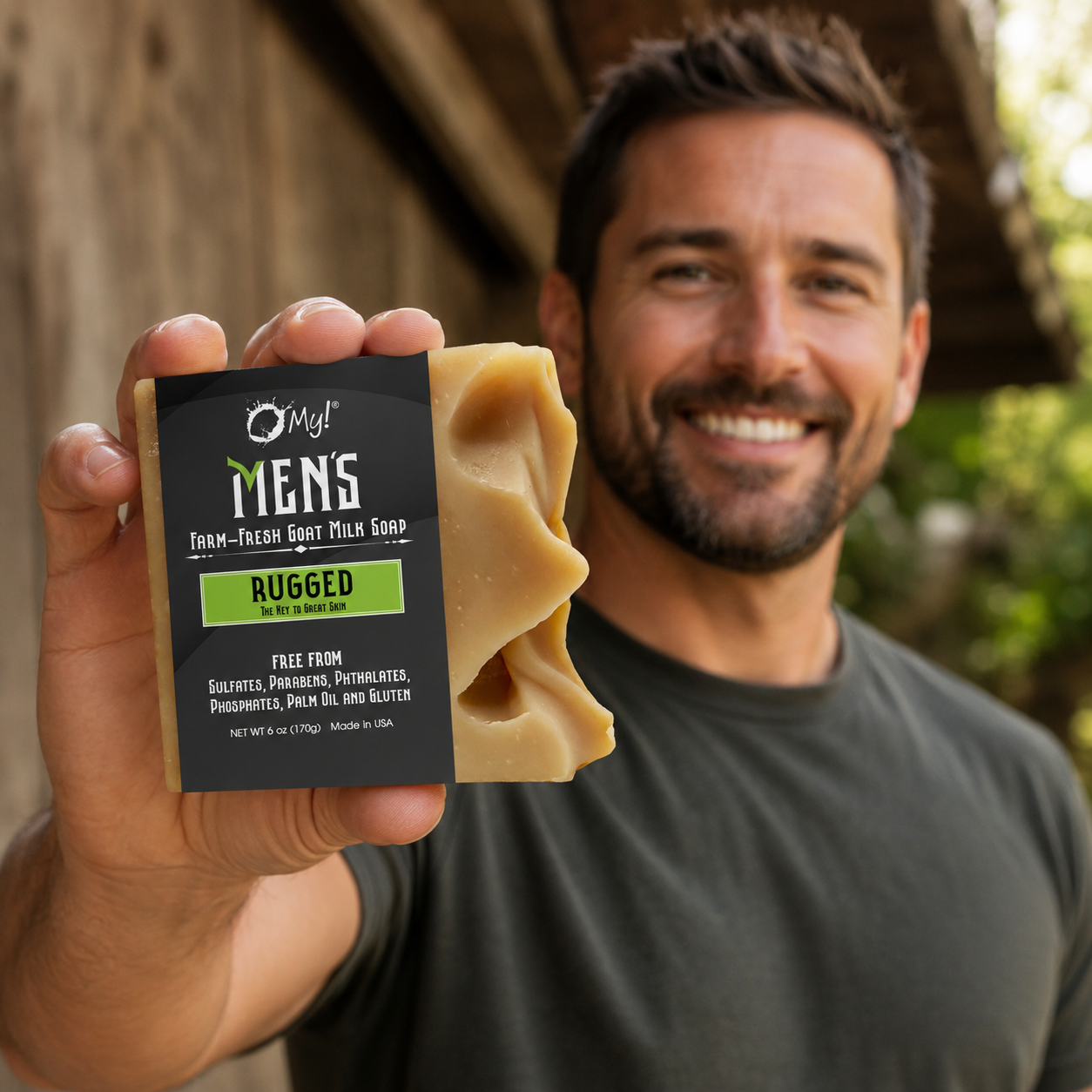 Man holding a bar of O My! Rugged Goat Milk soap in front of a outdoor, wooden background.