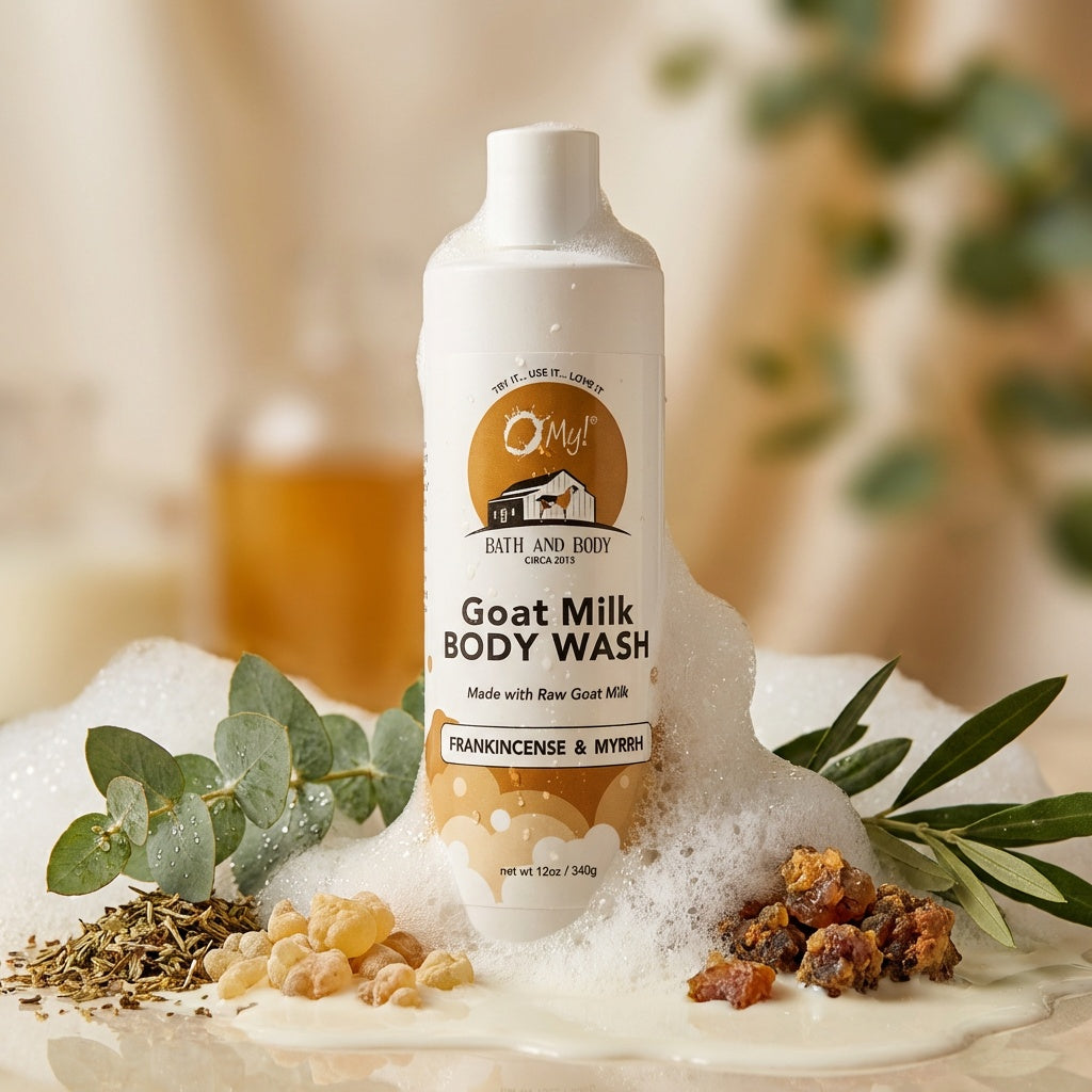 O My! Goat Milk Body Wash Frankincense and Myrrh bottle surrounded by green leaves and frankincense and myrrh stones on a milky background.